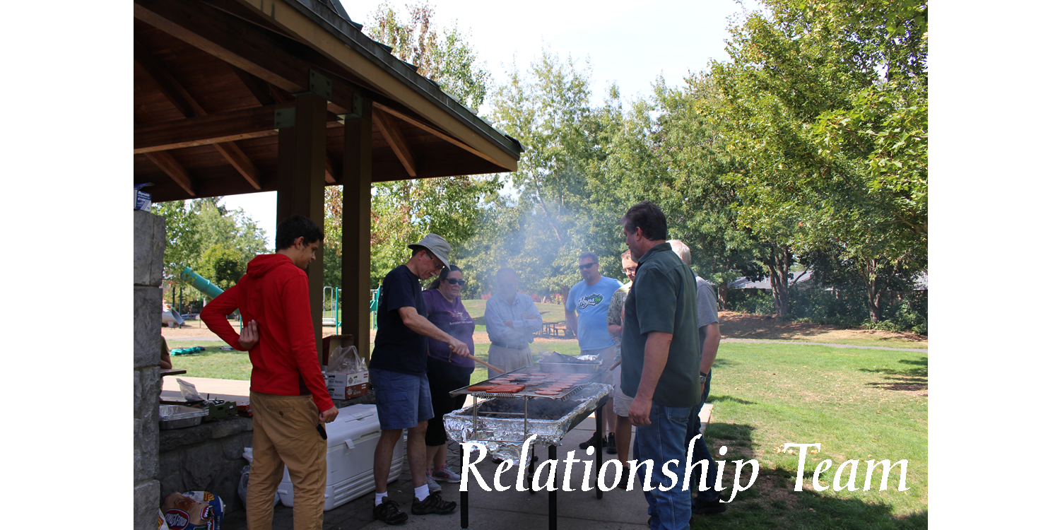 A group of people in a park grilling hot dogs and hamburgers while talking and the words "Relationship Team".