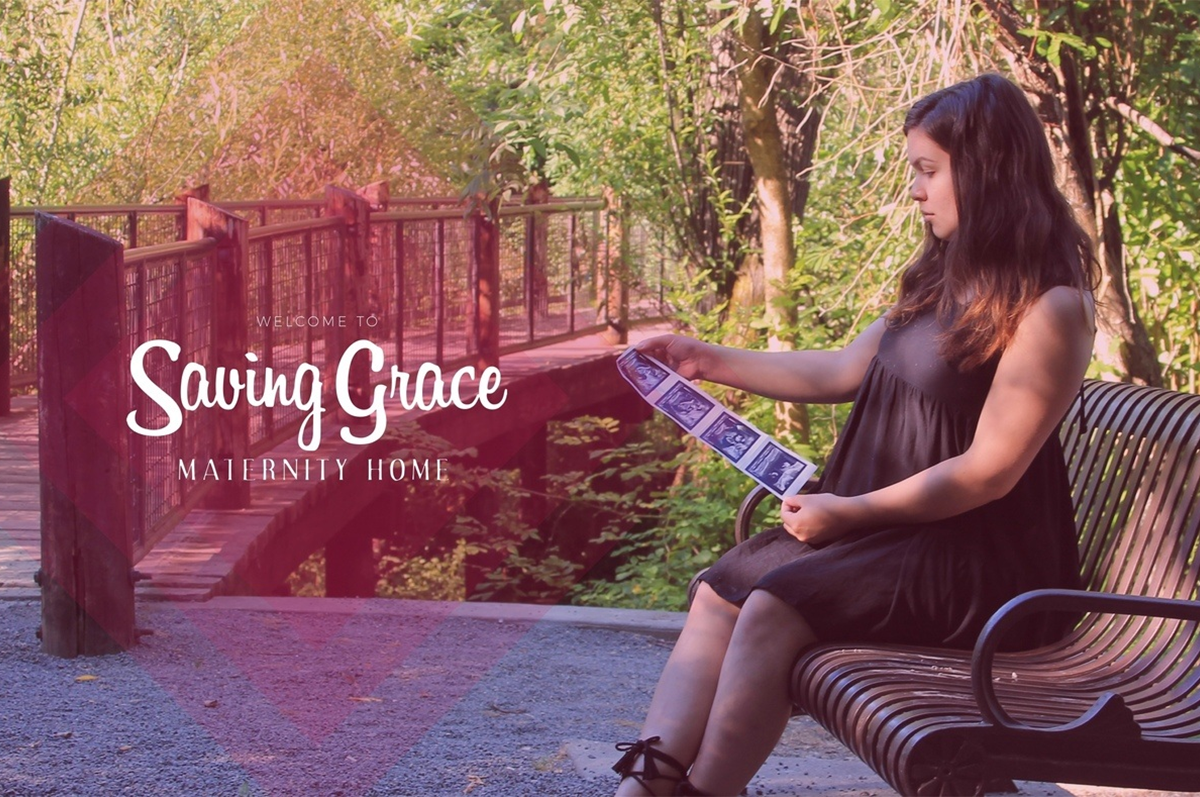 A woman looks at ultrasound pictures while sitting on a park bench near a bridge and the words "Saving Grace Maternity Home".